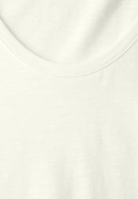 Gros plan sur un tissu blanc uni et doux montrant un col rond avec des coutures fines sur un T-shirt en coton lisse.