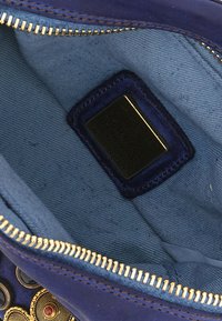 Interno di una borsa in pelle blu navy con rivestimento in tessuto azzurro, zip dorata e un'etichetta nera che riporta il marchio e i dettagli di produzione.