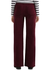 Bordeauxkleurige corduroy broek met een wijd model, voorzien van twee achterzakken en een gestructureerde stofafwerking. Gestreepte top zichtbaar.