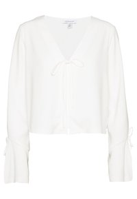 Blusa bianca corta con scollo a V e chiusura a fiocco davanti. Presenta maniche a campana con dettagli a fiocco ai polsini. Texture liscia.