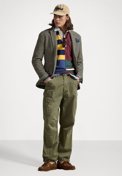 Tweedblazer, stripete flerfarget genser, oliven cargo bukser, brune slip-on sko, beige caps med logo, solbriller, brettet lommetørkle.
