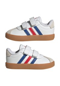 Zapatillas blancas con dos tiras de Velcro, con franjas laterales azules y rojas, detalles en gamuza gris y una suela de goma.
