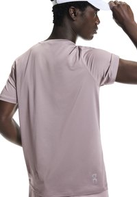 Vaaleanpunainen urheilupaita, jossa on sileä pinta, lyhyet hihat ja pyöreä pääntie; takana alhaalla hillitty logo.