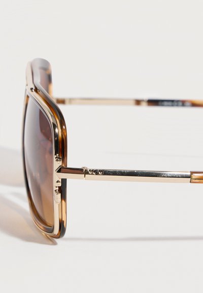 Γυαλιά ηλίου με καφέ σκουρόχρωμους ορθογώνιους φακούς και μεταλλικούς βραχίονες σε χρυσή απόχρωση πάνω σε λευκό φόντο.