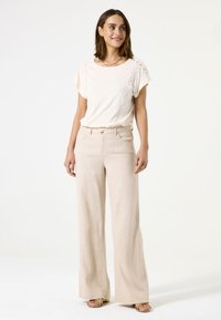 Top de tela suave crema con acentos de encaje, combinado con pantalones de pierna ancha beige de cintura alta. Sandalias planas completan el conjunto.