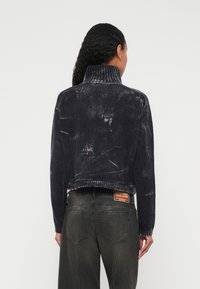 Īss tumši zils džemperis ar augstu apkakli, kam ir nodiluša izskata tekstūra un ribota apmale. Valkāts kopā ar tumši pelēnām džinsa biksēm ar redzamu etiķeti.