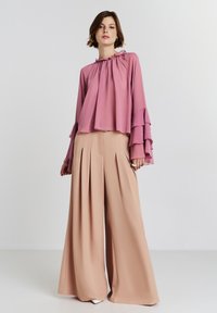 Blusa viola con maniche a volant, abbinata a pantaloni larghi beige con pieghe. Tessuto liscio con un design fluido.