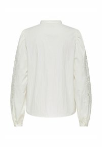 Biała bluzka z długimi, obszernymi rękawami z misternymi koronkowymi detalami na mankietach. Prosty kołnierzyk oraz zapięcie na guziki z tyłu.