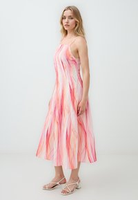 Une robe midi à motifs abstraits roses et rouges avec fines bretelles, en tissu léger, présentant une coupe décontractée et un ourlet évasé.