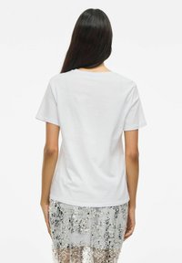 T-shirt blanc à manches courtes avec un col rond et une texture douce, associé à une jupe translucide ornée de sequins. Design minimaliste au dos.