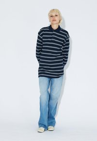 Navy striped long-sleeve polo shirt with a collared neckline, paired with light blue flared jeans and cream-colored shoes.