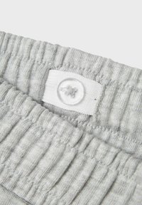 Grijze ribstof close-up met een wit label en een doorzichtige knop. De textuur is zacht en elastisch bij de tailleband.