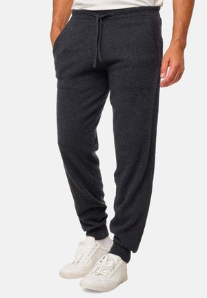 Pantalon de jogging noir en tissu doux, doté d'une taille élastique avec cordon de serrage, de poches latérales et de chevilles resserrées. Porté avec des baskets blanches.