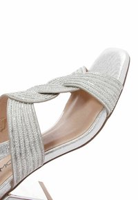 Sandale à talons argentés avec une tige texturée et un design à bandes croisées. Présente des accents scintillants et une forme de bout carré. Doublure intérieure lisse.