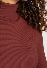 Brun ribbade polotröja med en tajt passform och texturerad tyg, med hög krage och långa ärmar.