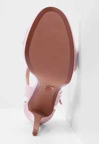 Semelle d'une sandale à talon haut rose avec un talon fin, une semelle extérieure lisse marron et une indication de pointure près de la voûte plantaire.