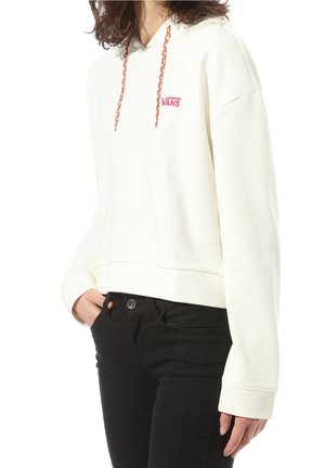 Felpa bianca corta con logo "VANS" rosa, dotata di cordini intrecciati multicolori e vestibilità rilassata. Indossata con jeans neri.