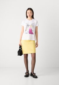 White t-shirt with a colorful graphic design, paired with a fitted yellow leather skirt, black tights, and black platform shoes.