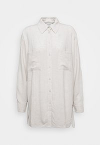 Camicia button-up in lino, colore beige chiaro, con colletto, due tasche frontali e maniche lunghe, caratterizzata da una vestibilità morbida e spacchi laterali.