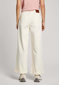 Breda ben, krämfärgade bomullbyxor med en något texturerad yta, med bakfickor och en brun läderpatch på midjebandet.