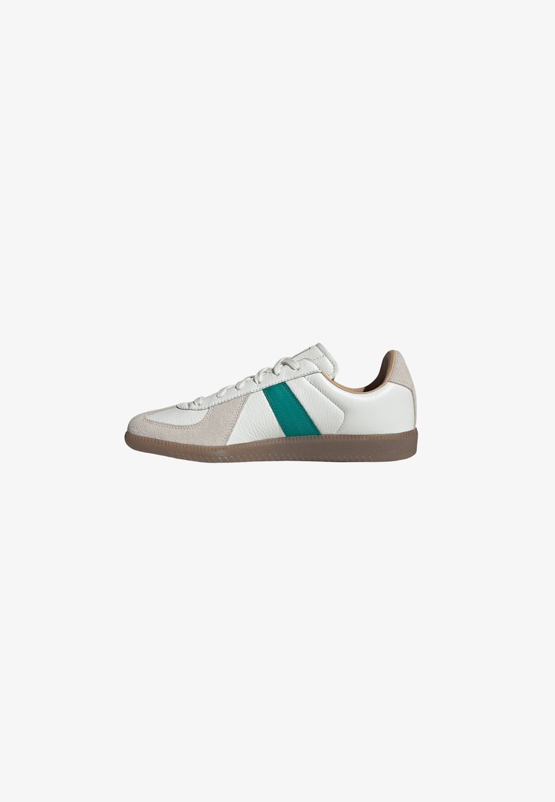 Baskets en cuir blanc avec des touches en daim beige, bande latérale verte et semelle en caoutchouc marron, présentées de profil.