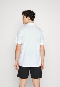 Hvid kortærmet polo t-shirt med krave, lavet af glat stof, set fra ryggen. Parret med sorte shorts.