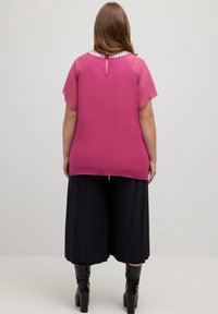 Chemisier rose transparent à manches courtes, doté d'un col rond et d'une ouverture en goutte d'eau dans le dos. Associé à un pantalon culotte plissé noir et des bottes montantes jusqu'aux genoux.