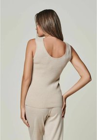 Beige geripptes Tanktop mit weitem Rundhalsausschnitt und figurbetontem Design, kombiniert mit passenden beigen Hosen, die eine glatte Textur aufweisen.