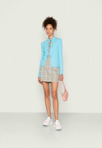 Cardigan de riscas em azul claro com detalhes de atar, combinado com uma saia curta xadrez. Ténis brancos e uma pequena mala rosa completam o visual.