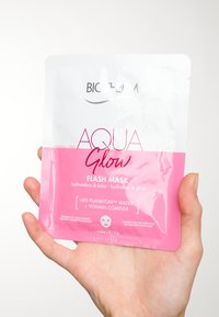 Biotherm Aqua Glow Flash Mask -pussi valkoisena ja vaaleanpunaisena; sisältää brändin logon, tuotteen nimen ja hyödyt, tekstin keskittyessä kosteutukseen.