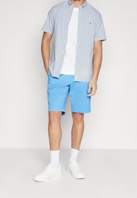Camicia a maniche corte a righe blu sopra una maglietta bianca, abbinata a pantaloni corti azzurri chiari e sneakers bianche.