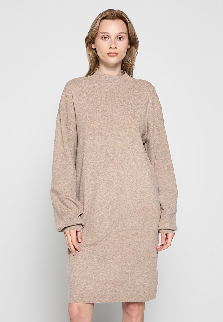 Beige Strickkleid mit langen, puffigen Ärmeln und hohem Kragen. Gerader Schnitt mit weicher Textur und durchgehendem Rippenmuster.
