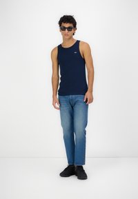 Top din bumbac de culoare albastru marin, asortat cu blugi drepti de culoare albastru deschis. Modelul poartă pantofi sport negri și ochelari de soare.