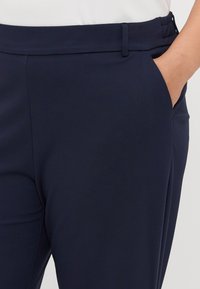 Granatowe spodnie o gładkiej fakturze, z pasa, kieszeniami bocznymi i dopasowanym krojem. Minimalistyczny design bez wzorów czy akcentów.