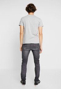 Camiseta gris de manga corta combinada con jeans ajustados de color gris oscuro. Costuras notables en los jeans y zapatillas negras estilo Vans visibles.