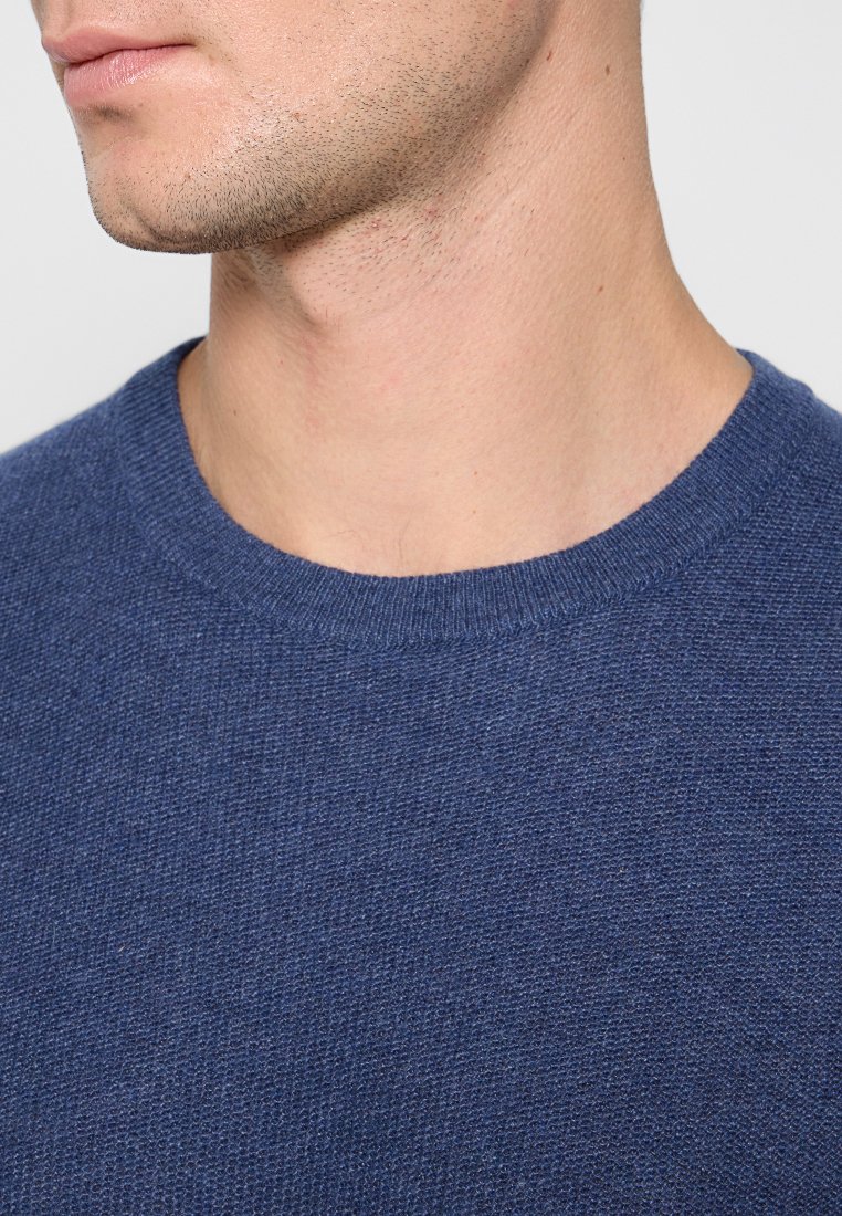 Maglione a maglia testurizzata blu navy con scollo rotondo. La ripresa ravvicinata mostra i dettagli sottili del tessuto e la forma nella zona del collo.