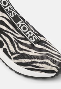 Baskets à enfiler avec une tige en maille à motif zèbre noir et blanc et une bande marquée "MICHAEL KORS" sur le dessus.
