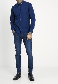 Námořnické modré košile na knoflíky s límečkem, dlouhými rukávy a bílými knoflíky, doplněné tmavě modrými džíny a černými botami.