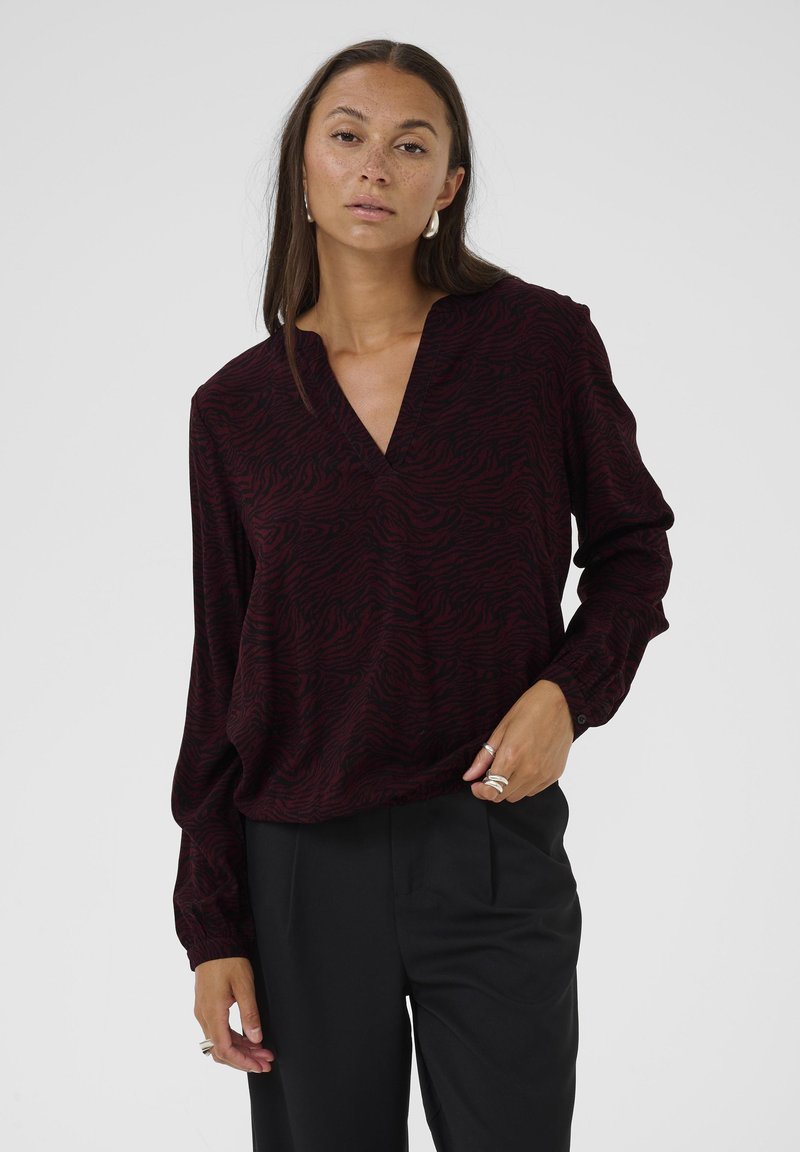 Blusa bordeaux con scollatura a V, maniche lunghe e motivo a strisce in rilievo, abbinata a pantaloni neri. Tessuto morbido, vestibilità comoda.