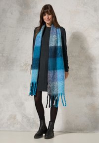 Sciarpa multicolore con tonalità di blu, grigio e turchese, caratterizzata da un design con frange. Tessuto morbido e testurizzato che si drappeggia elegantemente.