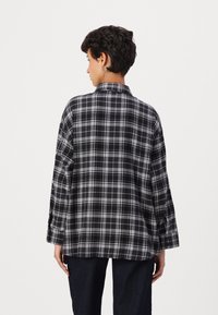 Black and gray plaid shirt made of soft fabric, featuring a collar, long sleeves with buttoned cuffs, and a relaxed fit. Back view.