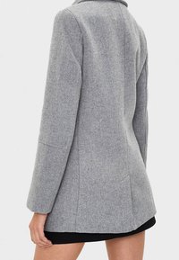 Grå kappa i ullblandning med långa ärmar, strikta axlar och slagkrage. Har en skräddarsydd passform och rena linjer. Ingen synlig hårdvara.