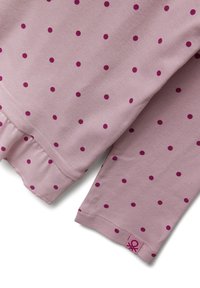 Roze langemouwtop met kleine magenta stippen, voorzien van een gerimpelde zoom en een logo etikette aan de onderkant links. Zacht katoenmateriaal.