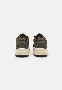 Olive green athletic shoes with a textured upper, featuring a cushioned beige sole and black accents on the heel and sides.