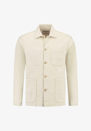 Heledbeez denimmerkk, millel on pikad varrukad, kaks esikotti ja heledad puitnupud. Omab klassikalist kraed ja minimaalselt peenitatud õmblusi.