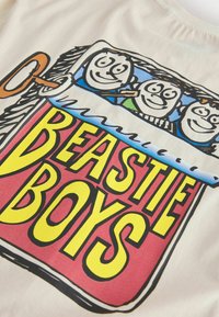 Trois visages dessinés sortant d'une boîte de conserve rouge, jaune et bleue étiquetée "BEASTIE BOYS" avec une clé de remontoir sur le côté.
