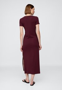 Robe mi-longue bordeaux à manches courtes, fente latérale et coupe ajustée. Confectionnée dans un tissu doux et lisse avec une texture unie.