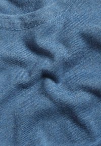 Strickstoff in Mittelblau, mit einer glatten Textur und subtilen Variationen. Der Ausschnitt ist ribbelig und zeigt sanfte Falten und Knicke.