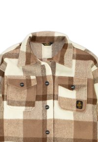Giacca a camicia a quadri marrone e crema realizzata in morbido fleece, con due tasche a patta, bottoni neri e un’etichetta con logo sul lato sinistro del petto.