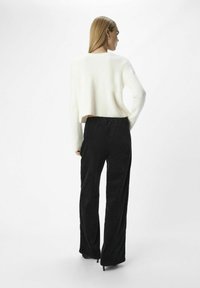 Avkortad vit ribbad tröja kombinerad med högmidjade svarta kordbyxor. Outfiten har en slät textur och en avslappnad passform.
